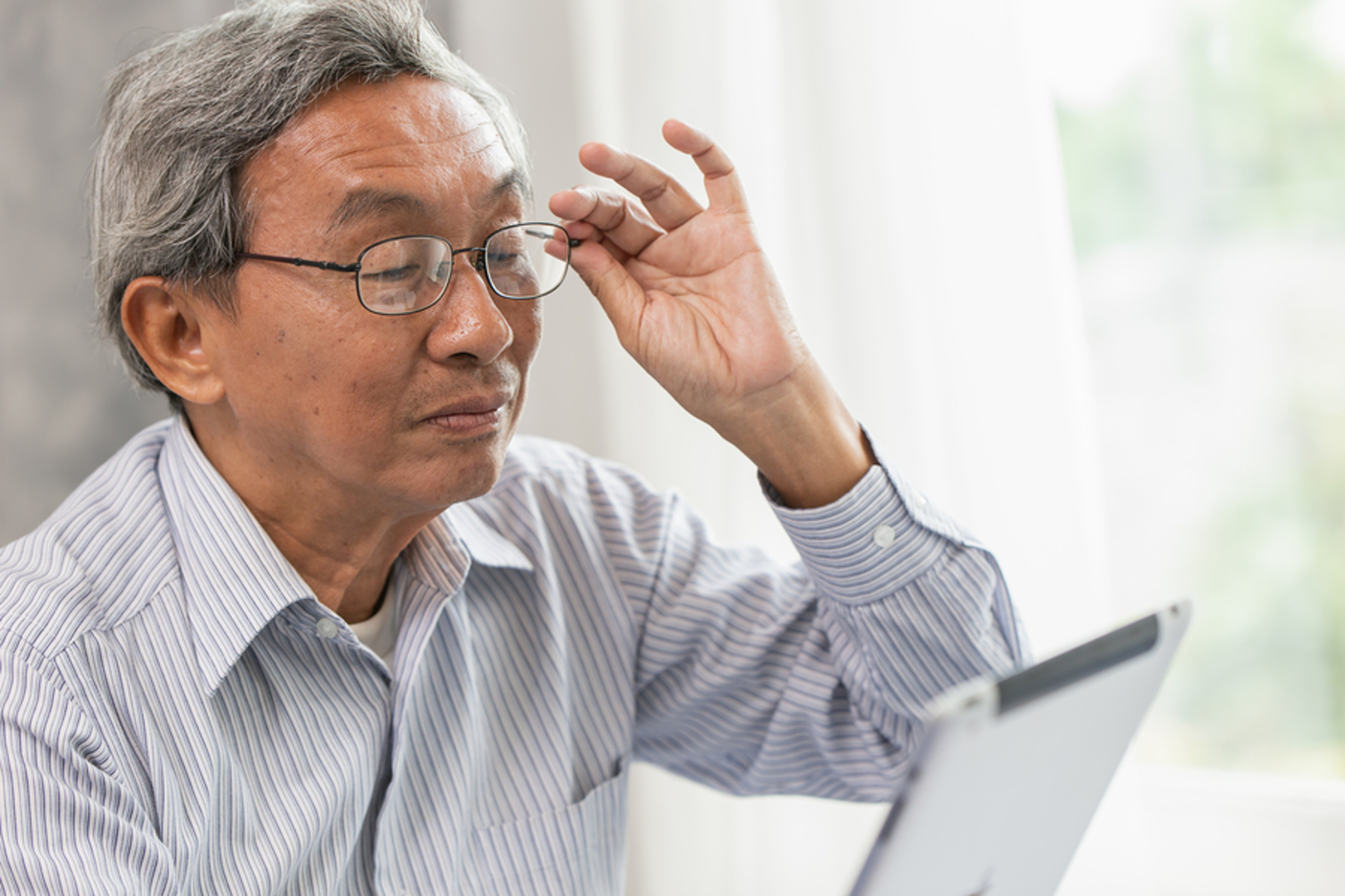 Man holding his glasses in one hand while reading his tablet.